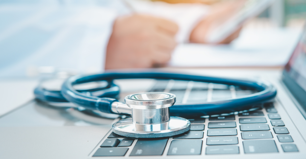 An Occupational Health Practitioner making notes during an occupational health management referral. A stethoscope sits on top of an open laptop.