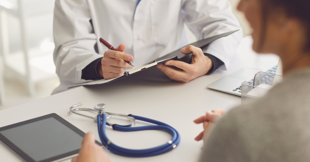 An occupational health practitioner going through a health questionnaire before a safety critical medical appointment. The practitioner and the person attending the medical appointment are both wearing shades of white. There is a blue stethoscope and a tablet on the table between them.