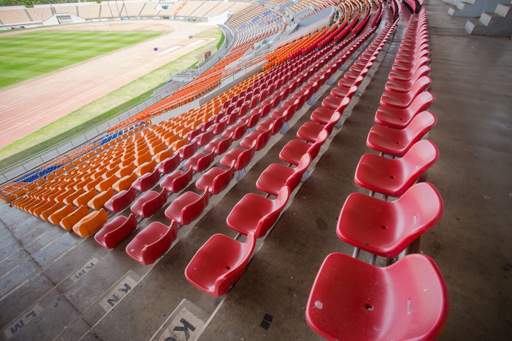 A sports stadium with a football pitch and athletics track with orange and red seats around the stadium.