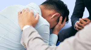 A man with his head in his hands being consoled by another man who has his hand placed on his upper back.