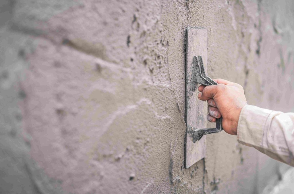 Close-up of a worker applying plaster to a rough concrete wall to create a smooth finish.