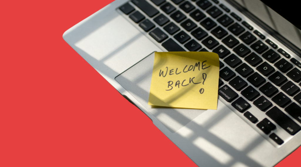 A laptop with a sticky note on it that says 'WELCOME BACK!' in front of a red background.