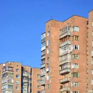 Tall, brick apartment buildings with many balconies and windows under a bright blue sky.