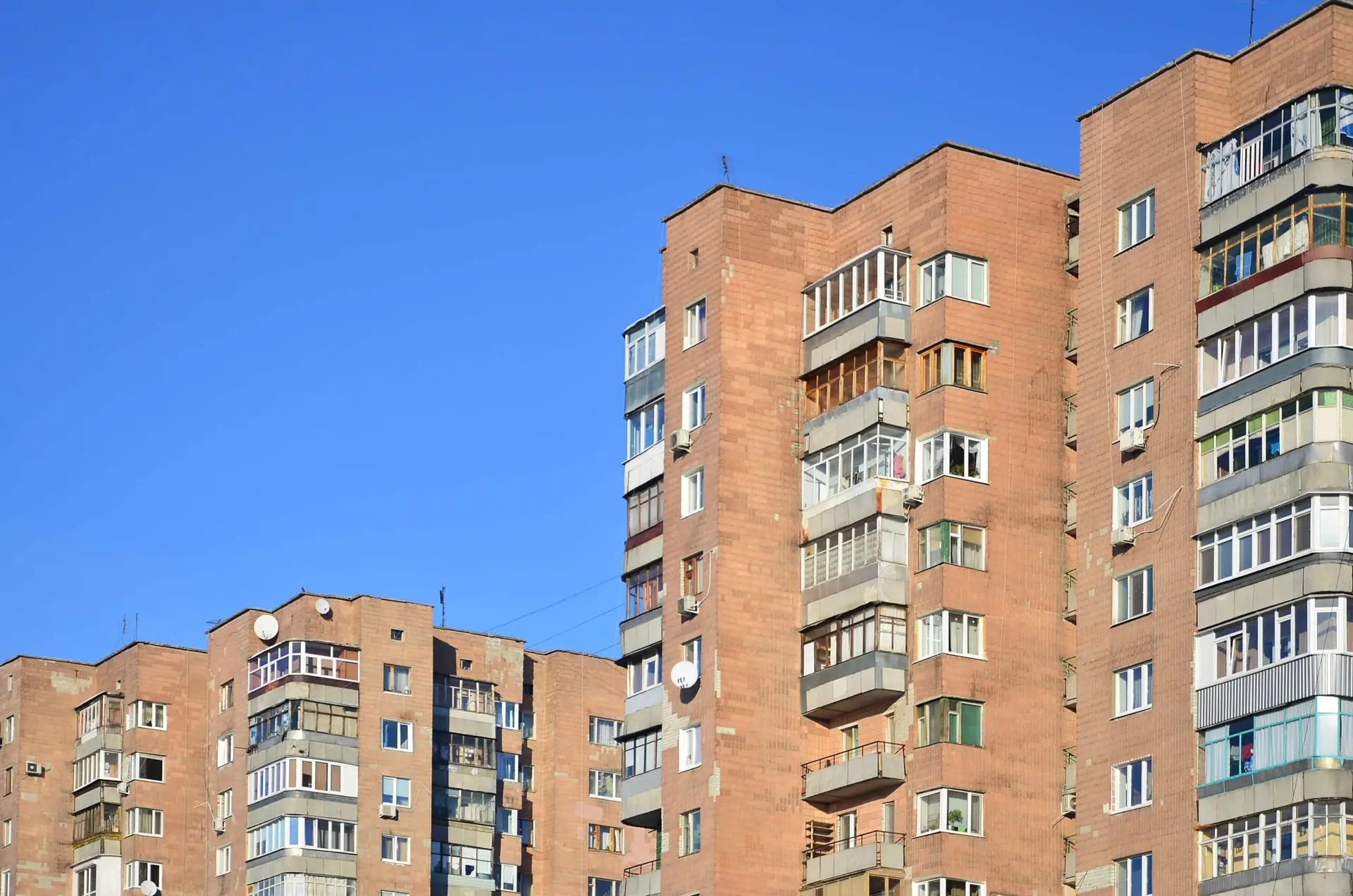 Tall, brick apartment buildings with many balconies and windows under a bright blue sky.