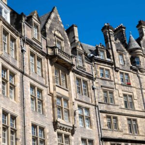 Historic stone building with ornate architectural details, tall windows, and steep gabled rooftops against a bright blue sky.