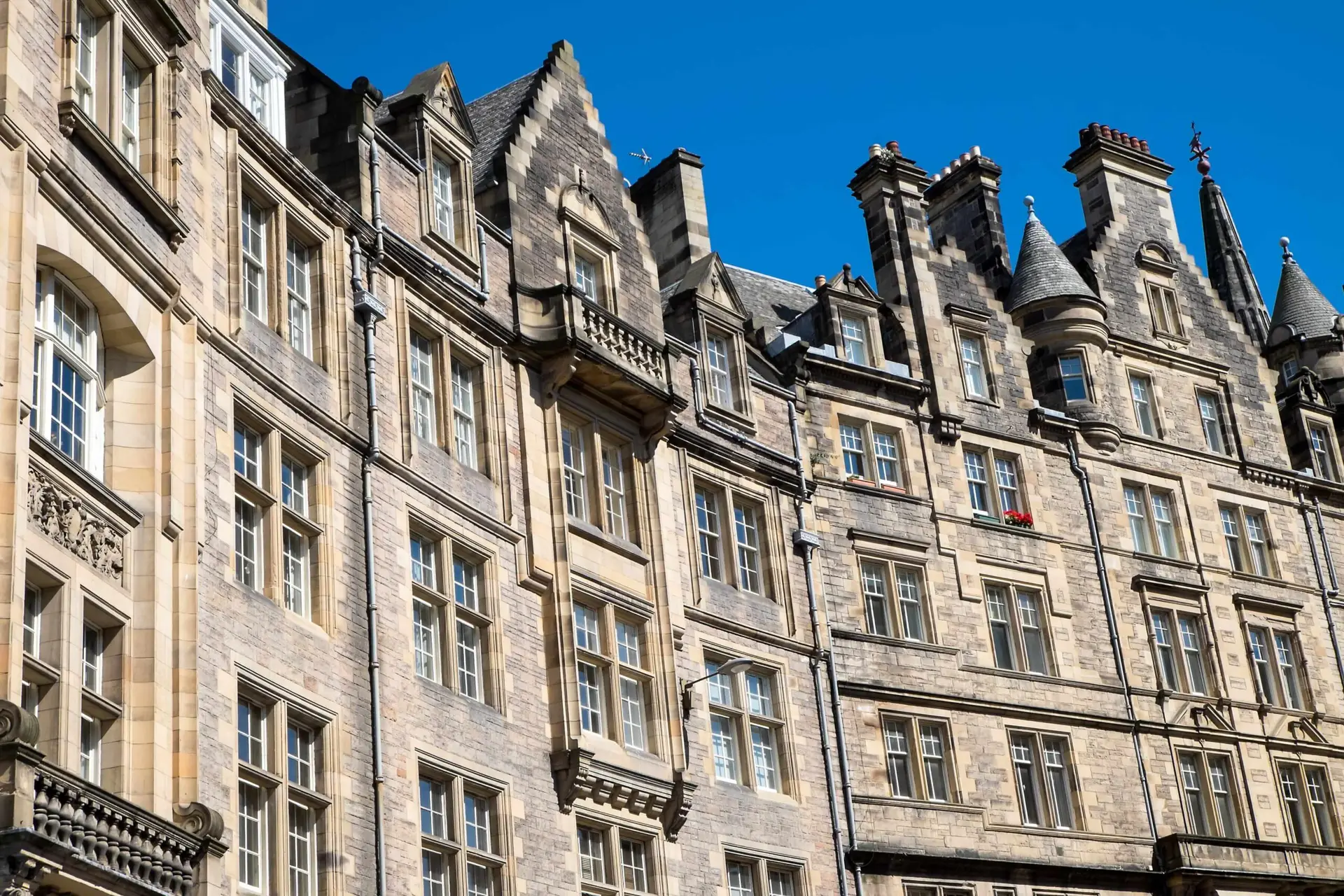 Historic stone building with ornate architectural details, tall windows, and steep gabled rooftops against a bright blue sky.