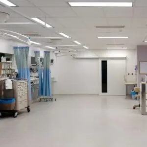 A clean, modern hospital ward with medical equipment, curtained treatment bays, storage units, and bright overhead lighting, designed for patient care and monitoring.