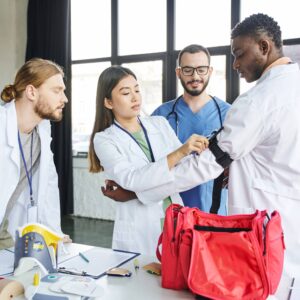 Medical professionals gathered around a table during a first aid training session, practicing the use of equipment and reviewing procedures with a colleague.