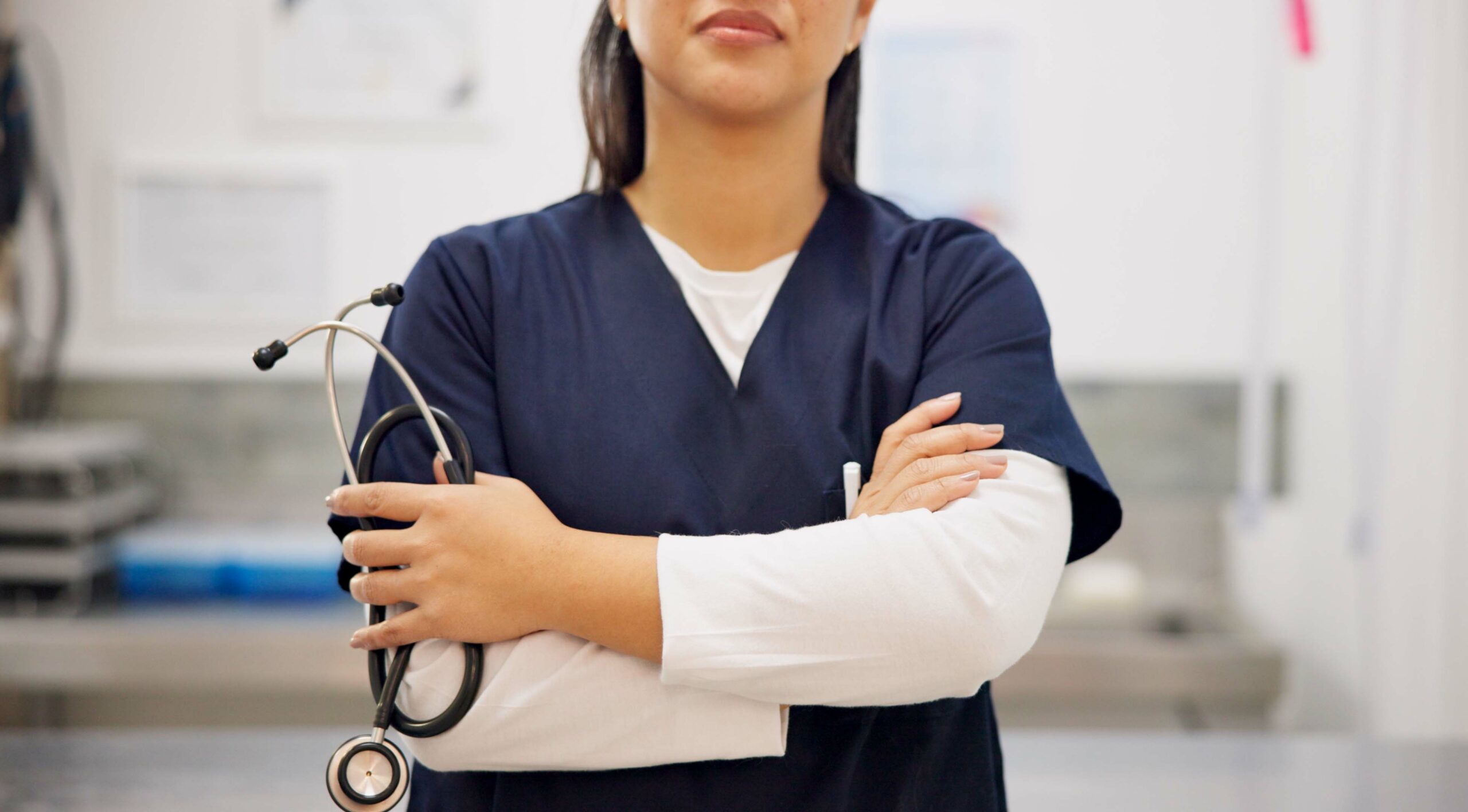 A close-up of a nurse with hands and arms crossed with a stethoscope in one hand, in a medical space