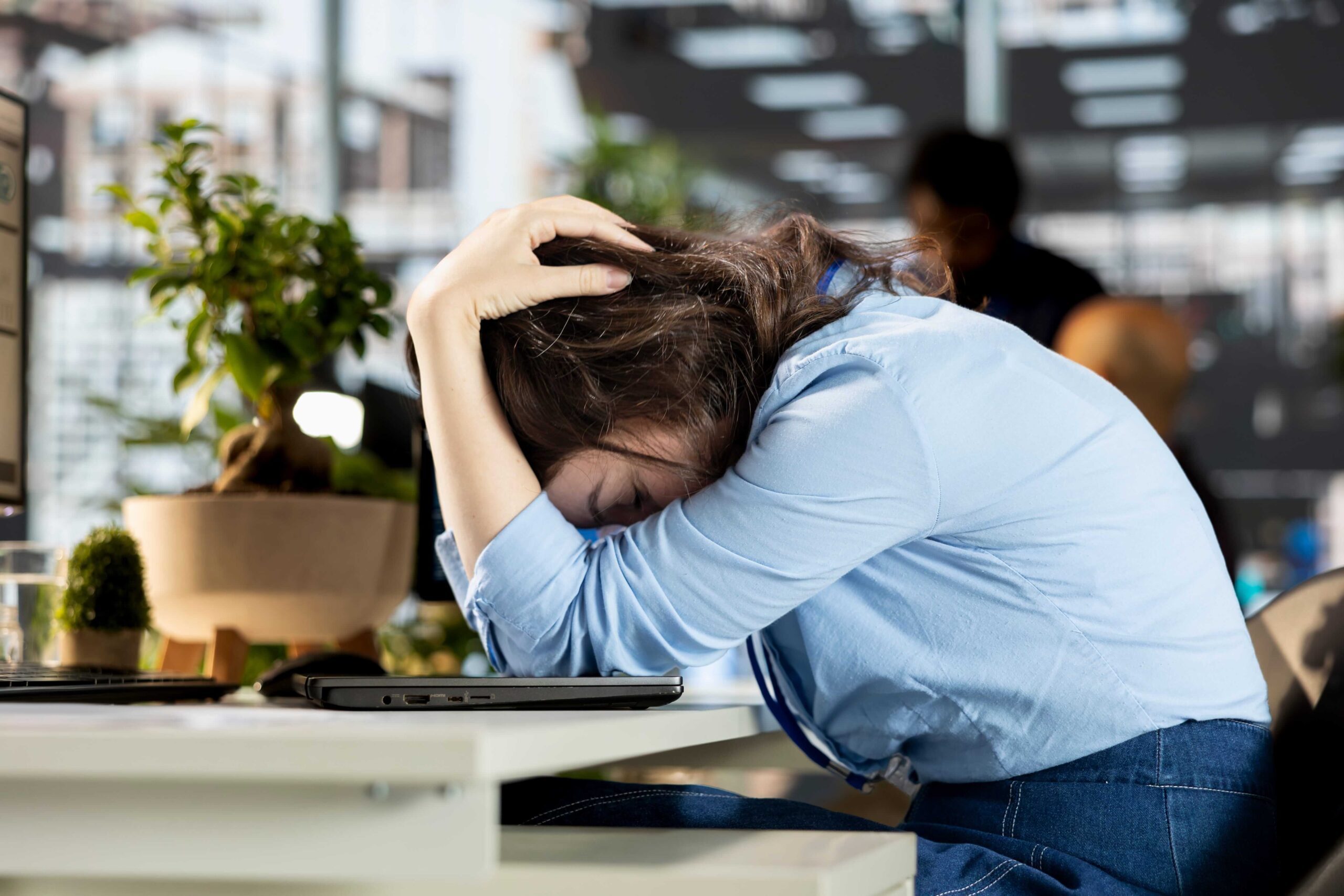 Stressed employee with head in hands at an office desk, showing signs of workplace pressure.