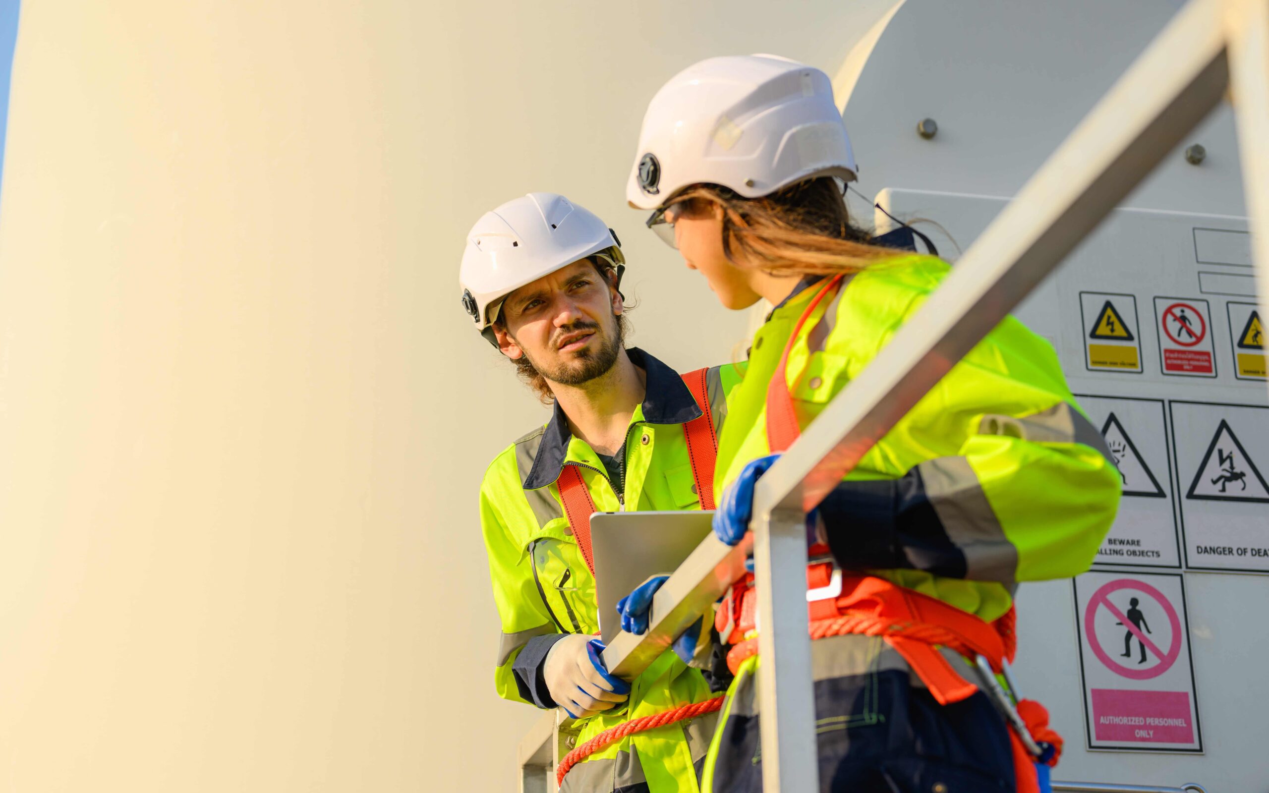 Two workers in high‑visibility PPE having a conversation beside warning signage at a worksite.